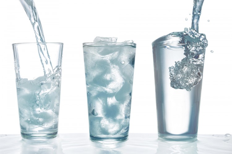 Drinking water being poured into glass with ice cubes